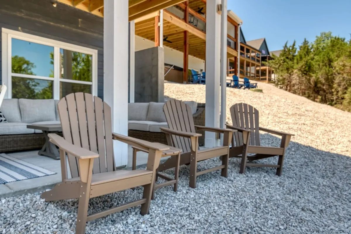 This inviting exterior scene features a set of Adirondack chairs arranged around a firepit on a gravel patio, suggesting a cozy gathering spot. The natural setting hints at social evenings spent sharing stories or enjoying s'mores under the stars.