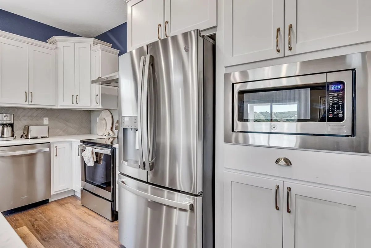 A modern kitchen with stainless steel appliances, white cabinetry, and a stone backsplash. The space is designed for both culinary creativity and socializing, with room for multiple people to cook, bake, and gather.