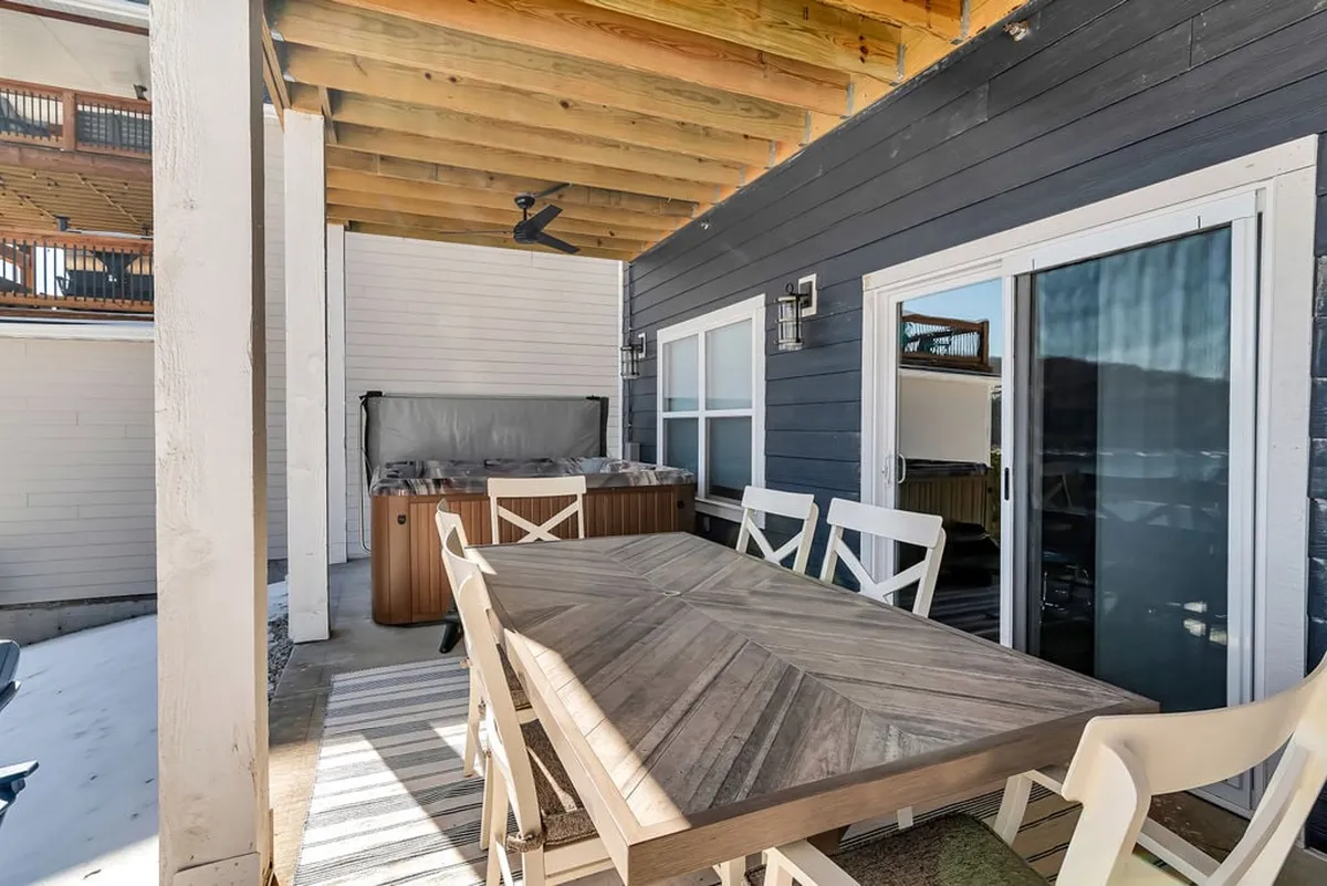 A casual and inviting outdoor space is depicted, with a dining table and a hot tub under a wooden ceiling. The setup encourages both socializing and relaxation, creating a seamless transition from active game nights to peaceful downtime.