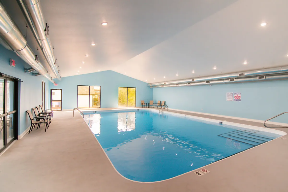 This image showcases a spacious indoor swimming pool area with large windows and modern seating, creating a cheerful and relaxed environment. The pool is inviting for both recreational swimming and socializing, and the space is designed for year-round enjoyment regardless of weather.