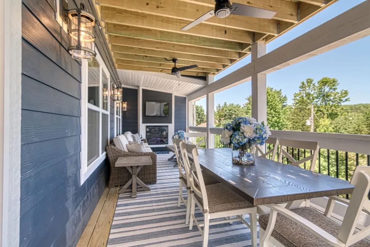 An expansive outdoor deck featuring a long dining table, blue floral centerpiece, comfortable seating, and decorative lanterns, all overlooking nature. This alfresco setting is ready for outdoor dining and relaxation with sweeping views.