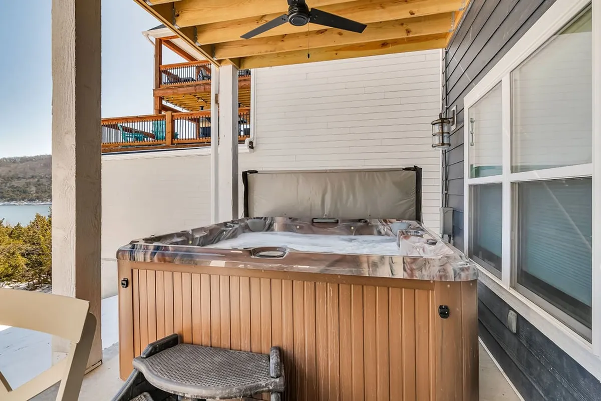 This image shows a tranquil outdoor deck featuring a private hot tub surrounded by natural scenery. Wooden decking and lush greenery create a serene setting, perfect for relaxing and enjoying the outdoors.