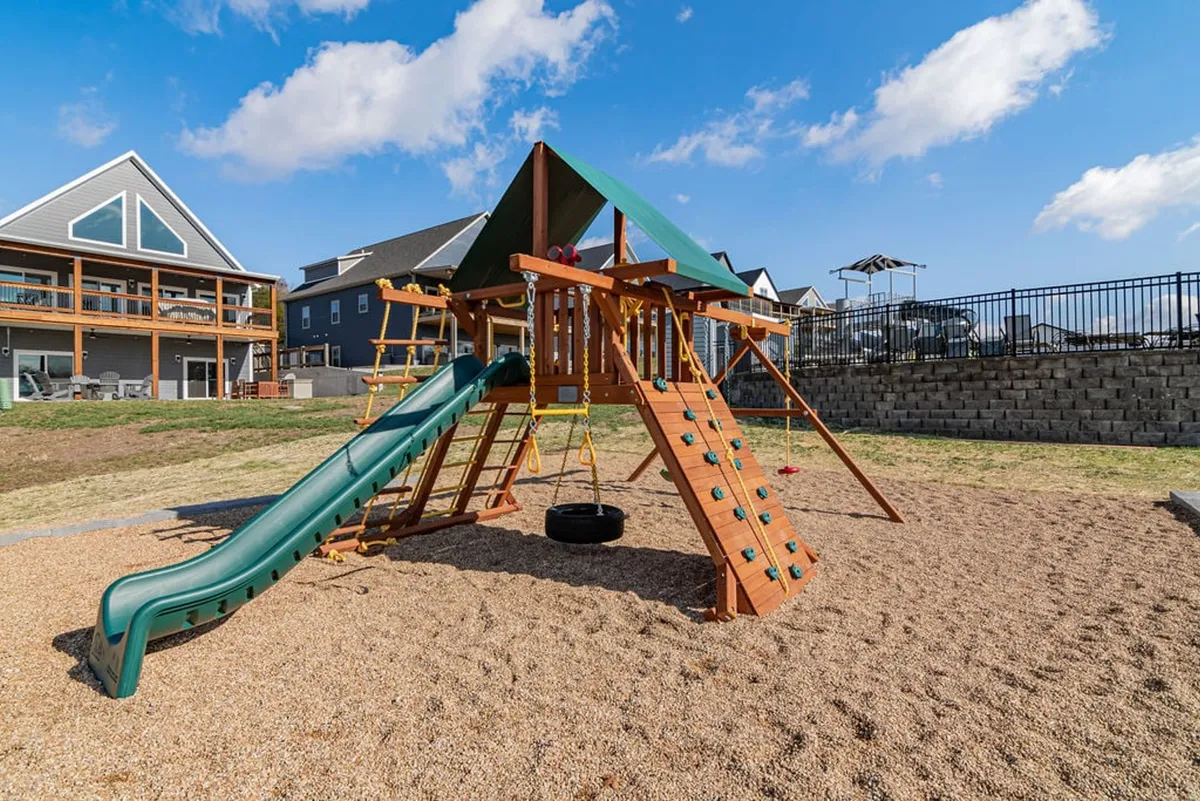 A cheerful exterior playground scene with slides, swings, and a backdrop of resort homes. Children can be seen playing, while families gather and enjoy the outdoors, illustrating a welcoming, family-oriented environment.