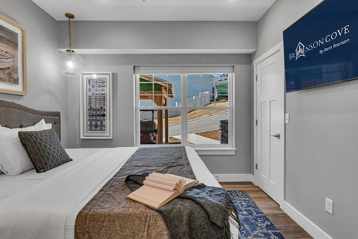 A serene bedroom featuring a plush bed adorned with decorative pillows, tasteful wall art, a window offering natural light, and charming bedside decor. The atmosphere is calm and inviting, perfect for relaxation and quiet moments.