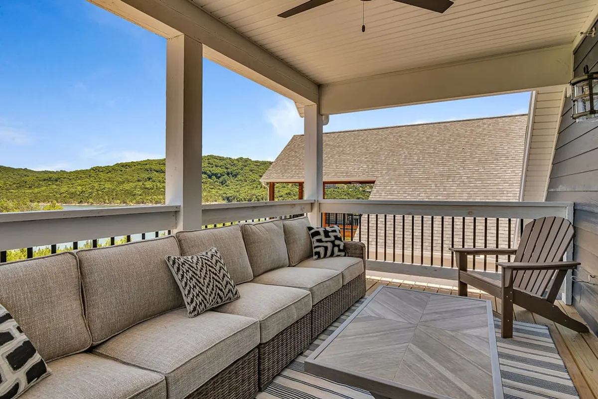This exterior image shows a comfortable outdoor sofa with decorative cushions, wooden furniture, and a stunning view of rolling hills. The seating area invites guests to relax and socialize while taking in the natural scenery, perfectly framing the tranquility and exclusivity of the setting.