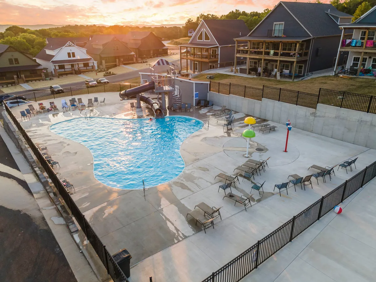An exterior scene featuring a vibrant outdoor pool complete with a water slide, lounge chairs, and a fun play structure. The setting is lively and sunlit, ideal for summer days and social gatherings by the water.