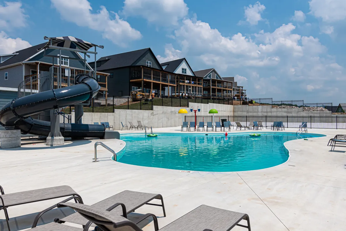 A vibrant outdoor swimming pool area featuring a twisting water slide, colorful lounge chairs, and umbrellas. Children can be seen having fun, while adults lounge nearby under the sun, capturing a lively, playful atmosphere.