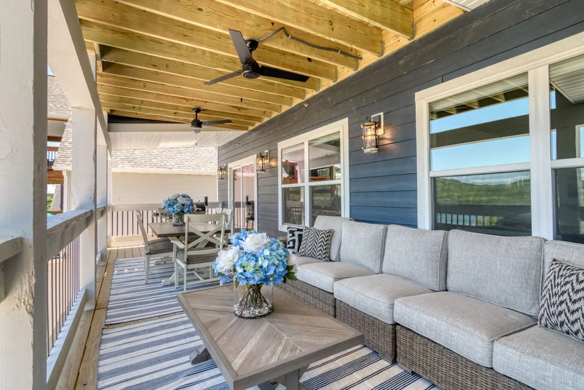 A stylish exterior living space is shown with a large sectional sofa, dining table and chairs, decorative flowers, and a ceiling fan. The area exudes comfort and is ideal for both relaxation and social gatherings, while also highlighting opportunities for al fresco dining and outdoor enjoyment.