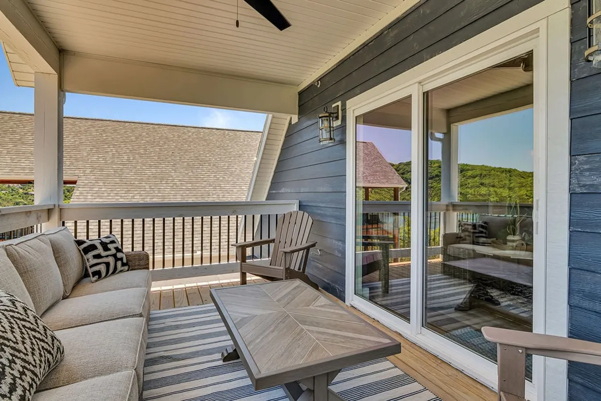 This image features a cozy exterior seating area with comfortable chairs and patterned cushions, overlooking scenic views through large glass doors. It evokes a sense of serenity and connection with the outdoors, ideal for relaxing moments at any time of day.