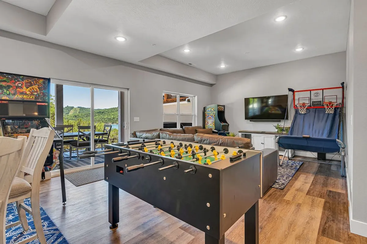 A vibrant game room featuring a foosball table, arcade machines, a basketball hoop, and a comfortable seating area. The space exudes a lively, fun atmosphere perfect for friendly competition and group relaxation.