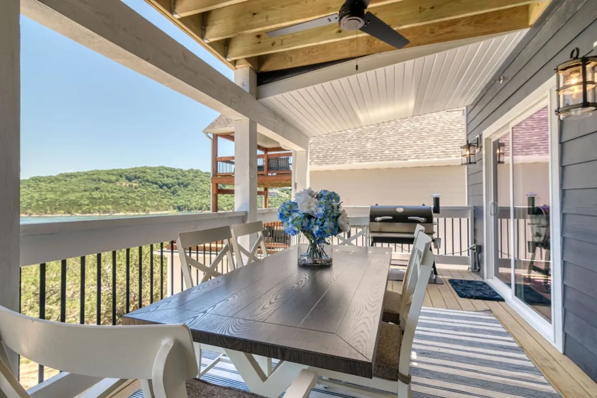An exterior dining area with a table set for a meal, a blue flower arrangement, and a premium grill in the background. The setting overlooks rolling hills, inviting guests to enjoy outdoor cookouts and gatherings.