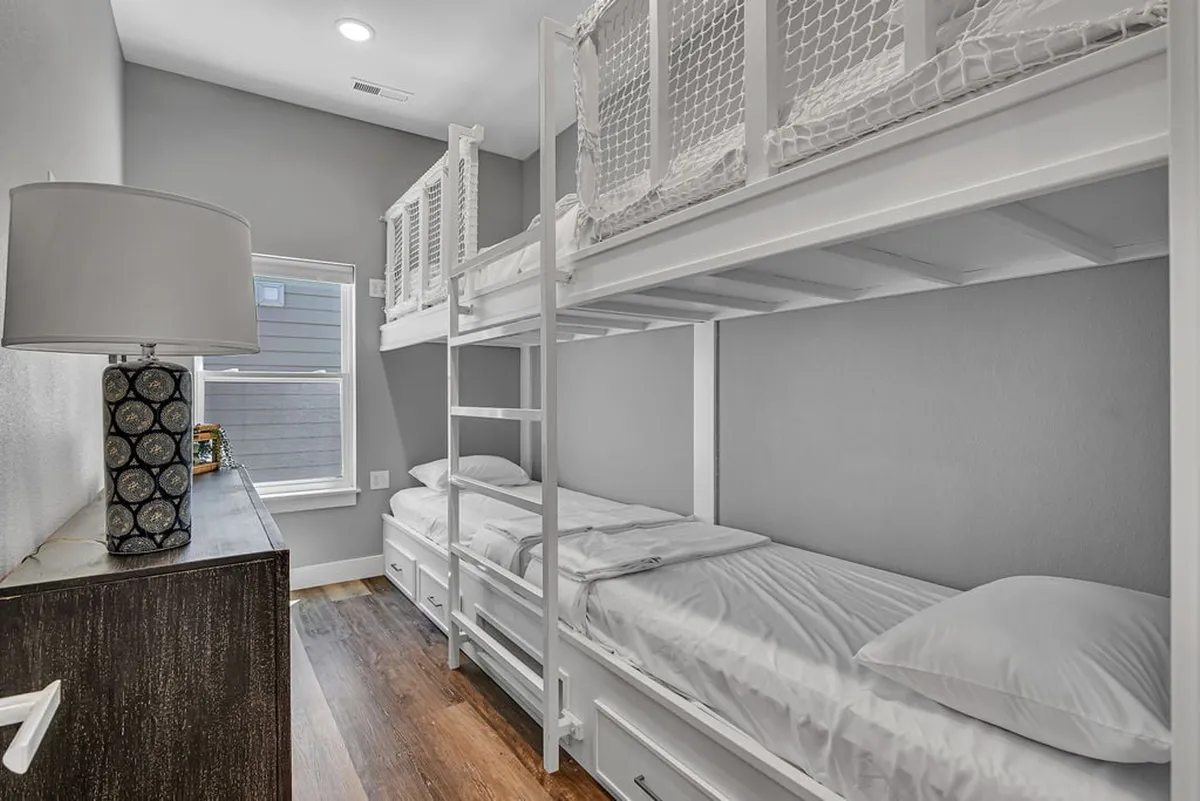 A cozy bunk room with neatly arranged bunk beds, a soft lamp, and a practical dresser. The room is inviting and playful, ideal for children or groups, and hints at flexible sleeping arrangements.