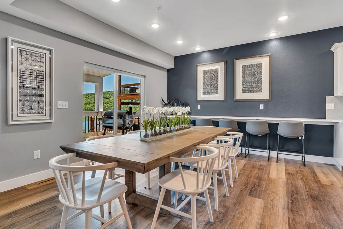 A spacious dining area boasting a large wooden table with a decorative plant centerpiece, flanked by framed artwork and bathed in natural light from nearby windows. The setting encourages family-style meals and celebrations.